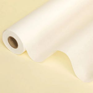 May include: A roll of off-white paper, partially unrolled, revealing a soft, textured surface. The paper is rolled around a brown cardboard core. The background is a pale yellow.