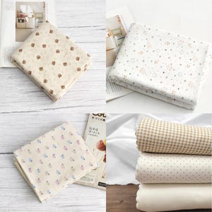 Könnte beinhalten: Eine Sammlung gefalteter Stoffmuster mit verschiedenen Mustern. Die Muster umfassen Bären, Sterne, kleine Blumen und Tupfen. Die Stoffe sind in neutralen Farben wie Beige, Weiß und Hellbraun gehalten.