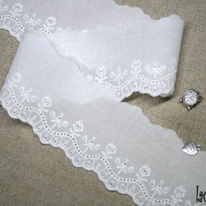 May include: White cotton lace trim with a scalloped edge and delicate floral embroidery. The lace is approximately 1 inch wide.