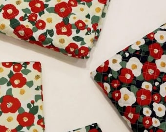May include: Quilted fabric pieces featuring a floral pattern of red and white camellia flowers with green leaves. The fabric is available in two colorways: one with a cream background and one with a dark black background, both with a grid stitch.
