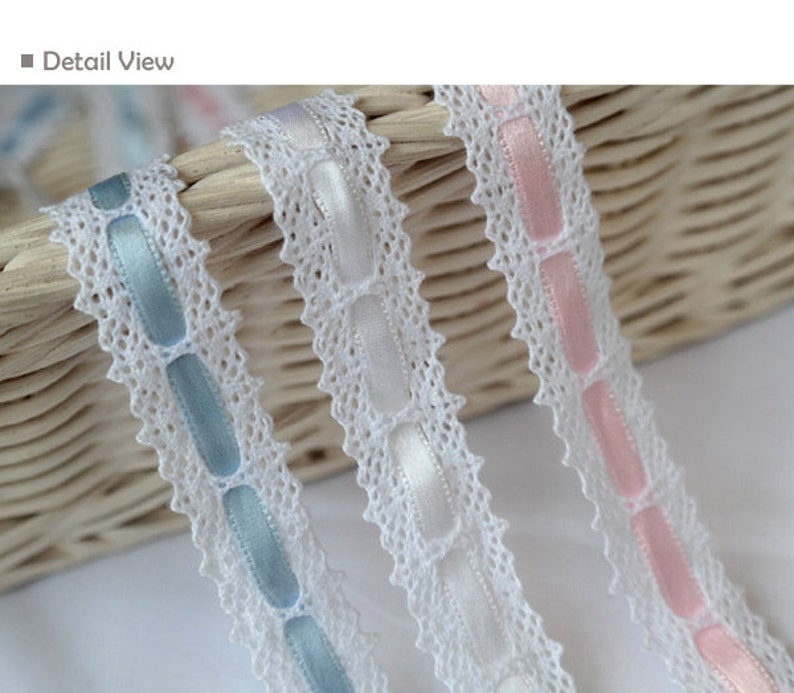 May include: Three white lace trims with different coloured satin ribbon accents. The trims feature a repeating pattern of oval shapes. The ribbons are light blue, white, and pink.