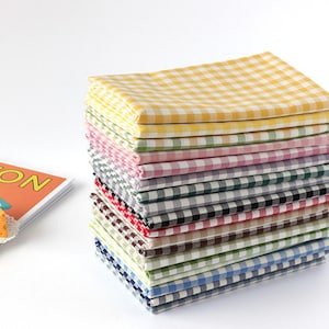 Peut inclure: Une pile de serviettes en tissu à carreaux colorés, dans des tons de jaune, vert, rose, gris, noir, marron et bleu. Les serviettes sont soigneusement pliées et empilées, créant une présentation visuellement attrayante. Le tissu présente un motif vichy classique.