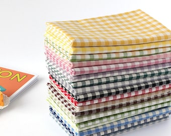 May include: A stack of colorful checkered fabric napkins in various colors, including yellow, green, pink, gray, black, brown, and blue. The napkins are neatly folded and stacked, creating a visually appealing display. The fabric has a classic gingham pattern.