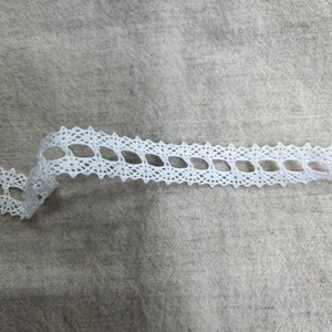 May include: White lace trim featuring a delicate diamond pattern. The trim is made from a soft, lightweight material and has a slightly scalloped edge.
