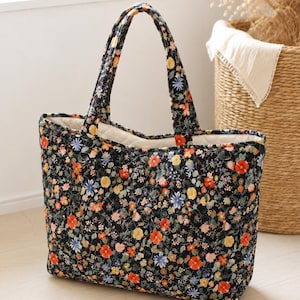Pu&ograve; includere: Una borsa tote trapuntata con sfondo nero e un denso motivo floreale colorato nei toni del rosso, giallo e blu. La borsa presenta due manici in tessuto abbinato e una fodera interna color crema con una texture trapuntata a rombi.