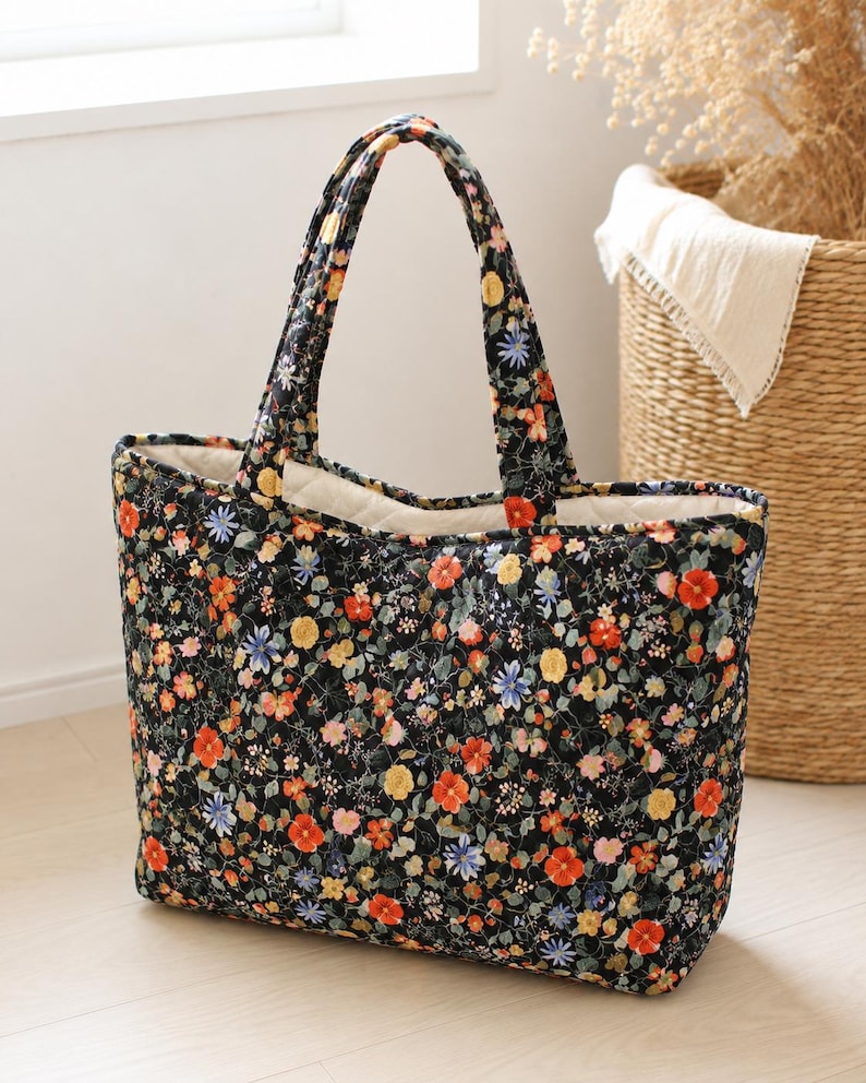 Pu&ograve; includere: Una borsa tote trapuntata con sfondo nero e un denso motivo floreale colorato nei toni del rosso, giallo e blu. La borsa presenta due manici in tessuto abbinato e una fodera interna color crema con una texture trapuntata a rombi.
