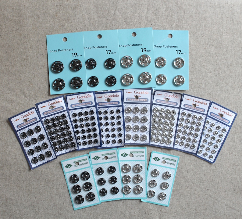 May include: Assortment of silver and black snap fasteners in various sizes, packaged on cards labelled "Gondola Snap Fasteners". The cards show the size of the fasteners in millimetres, such as 17mm and 19mm.
