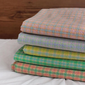 Peut inclure: Un empilement de quatre échantillons de tissu à carreaux de différentes couleurs, dont le rose, le vert, le jaune et le bleu. Le tissu a un motif à carreaux.