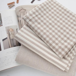 May include: Four pieces of fabric in different patterns: a beige and white gingham, a beige and white striped, a plain beige, and another beige and white striped fabric.