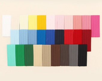 May include: A collection of rectangular fabric swatches arranged in three horizontal rows, displaying a wide spectrum of solid colors including white, yellow, pink, blue, red, green, brown, gray, and black, each featuring vertical stitched lines.