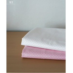 May include: Two folded pieces of fabric stacked on top of each other. The top piece is white with small pink polka dots, and the bottom piece is pink with small white polka dots. The fabric has a smooth texture and a consistent pattern throughout.