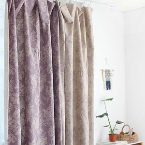 K&ouml;nnte beinhalten: Bodenlange Vorh&auml;nge mit einem sich wiederholenden Blumenmuster in gedeckten Violett- und Beiget&ouml;nen. Der Stoff h&auml;ngt an einer wei&szlig;en Stange mit kreisf&ouml;rmigen Ringen und bildet vertikale Falten. Das Design zeigt einen durchgehenden botanischen Druck.