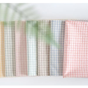 May include: A set of eight fabric swatches in various pastel colours with a small checkered pattern. The swatches are arranged in a row from left to right, with the yellow swatch on the left and the pink swatch on the right.
