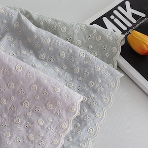 Könnte beinhalten: Nahaufnahme von drei pastellfarbenen bestickten Stoffen. Die Stoffe sind hellviolett, hellblau und hellgrün. Jeder Stoff hat einen gewellten Rand und ist mit weißen, gestickten Blumenmustern verziert.