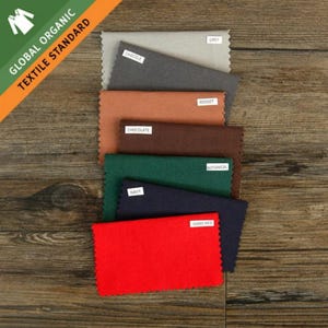 May include: A set of seven rectangular fabric swatches with pinked edges, labeled with the colors Grey, Chacole, Rosset, Chocolate, Botanical, Navy, and Mars Red. The swatches are stacked vertically and feature a Global Organic Textile Standard logo.