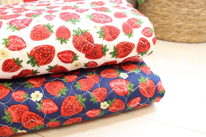 Pu&ograve; includere: Due pezzi di tessuto trapuntato piegati e impilati l'uno sull'altro. Il tessuto superiore &egrave; bianco con un motivo ripetuto di fragole rosse e piccoli fiori gialli. Il tessuto inferiore &egrave; blu navy con lo stesso motivo di fragole e fiori.