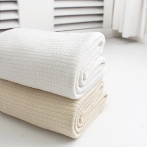 Peut inclure: Deux couvertures pliées, une blanche et une beige, avec une texture en nid d'abeille. Les couvertures sont empilées l'une sur l'autre.