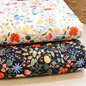 Pu&ograve; includere: Due coperte trapuntate piegate con un motivo floreale. La coperta superiore ha uno sfondo bianco con fiori rossi, gialli e blu. La coperta inferiore ha uno sfondo nero con la stessa stampa floreale, che include foglie e steli di colore verde.