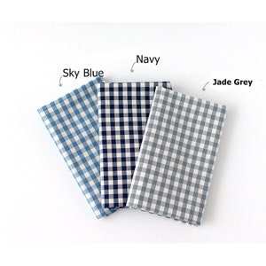 May include: Three folded fabric squares in Sky Blue, Navy, and Jade Grey, each featuring a classic gingham pattern. The fabric is arranged on a white surface, with labels indicating the color of each square. The Sky Blue square is on the left, the Navy in the middle, and the Jade Grey on the right.