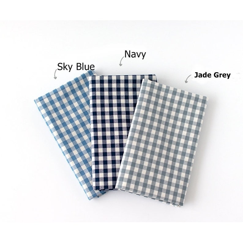 May include: Three folded fabric squares in Sky Blue, Navy, and Jade Grey, each featuring a classic gingham pattern. The fabric is arranged on a white surface, with labels indicating the color of each square. The Sky Blue square is on the left, the Navy in the middle, and the Jade Grey on the right.