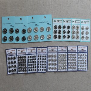 May include: Assortment of silver and black snap fasteners in various sizes, packaged on cards labelled "Snap Fasteners" and "Gondola". The cards show the size of the fasteners in millimetres, such as 17mm and 19mm.