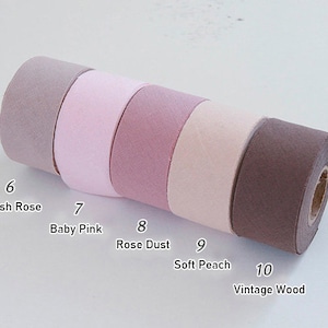 May include: Five rolls of fabric ribbon arranged in a row, labelled with numbers and names: 6 Ash Rose, 7 Baby Pink, 8 Rose Dust, 9 Soft Peach, and 10 Vintage Wood. The ribbons feature a textured, matte finish in various shades of pink, mauve, and brown.