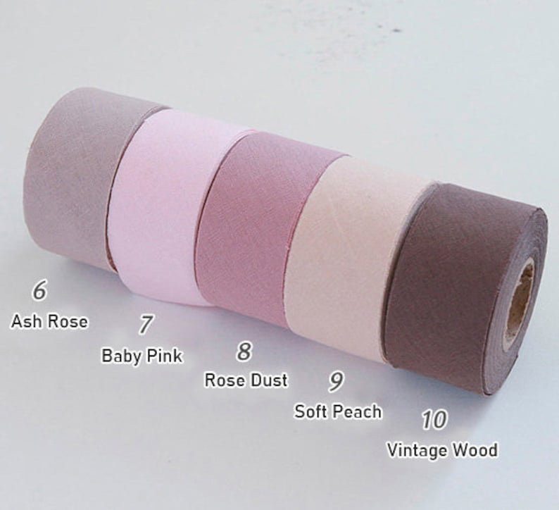 May include: Five rolls of fabric ribbon arranged in a row, labelled with numbers and names: 6 Ash Rose, 7 Baby Pink, 8 Rose Dust, 9 Soft Peach, and 10 Vintage Wood. The ribbons feature a textured, matte finish in various shades of pink, mauve, and brown.