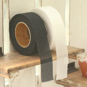 Puede incluir: Dos rollos de cinta de gancho y bucle negra y blanca. La cinta está en un estante de madera.