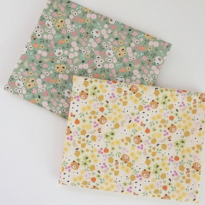 May include: Two fabric swatches with a floral pattern. One swatch is green with white and pink flowers and the other is yellow with white and orange flowers. Both fabrics feature small bear faces.