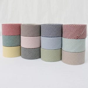 Peut inclure: Une collection de douze rouleaux cylindriques de ruban en tissu disposés sur trois rangées. Chaque rouleau présente un motif à petits carreaux vichy dans diverses couleurs, notamment rouge, vert, jaune, rose, noir, bleu et beige.