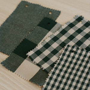 May include: Four fabric swatches in different patterns. The first swatch is a solid dark green, the second is a black and white gingham, the third is a black and white gingham with a larger check, and the fourth is a black and white gingham with a smaller check.