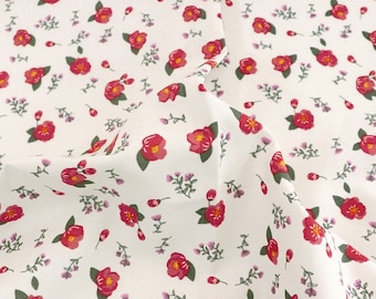 May include: A white fabric featuring a repeating floral pattern of small pink and red camellia-style blossoms with yellow centers, accompanied by tiny green leaves and delicate purple sprigs scattered across the surface in a dense, uniform arrangement.