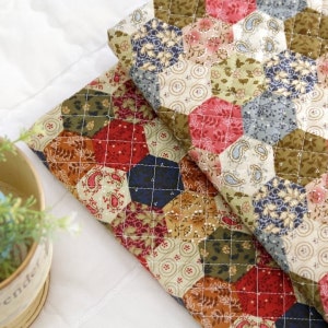 Peut inclure: Deux morceaux de tissu avec un motif patchwork présentant des formes hexagonales de différentes couleurs, notamment rouge, vert, bleu et marron. Le tissu est matelassé avec un motif en losange.