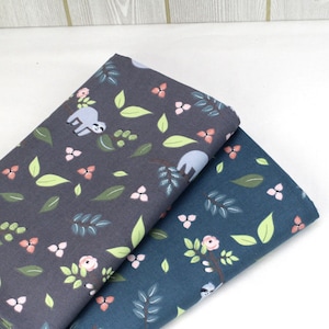 May include: Two folded pieces of fabric featuring a repeating pattern of sloths, green leaves, and small pink flowers. One piece is dark charcoal gray, and the other is a deep blue. The fabric displays a smooth, woven texture with a matte finish.