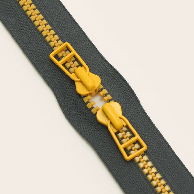 May include: A close-up of a zipper with a dark gray tape and yellow teeth. The zipper is open and the slider is visible.
