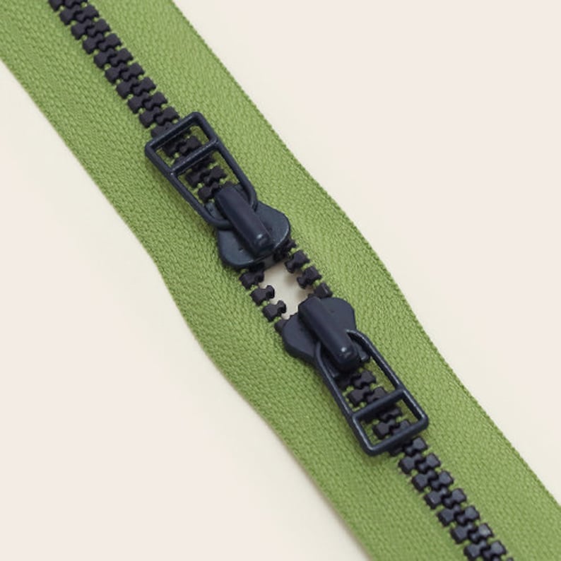May include: A green zipper with two black plastic pull tabs. The zipper is open and the teeth are visible.
