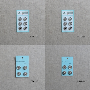 May include: Four packs of silver snap fasteners in different sizes: 12mm, 14mm, 17mm, and 19mm. Each pack has a blue label with the text "Snap Fasteners" and the size of the fasteners in millimetres.