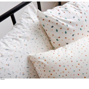 Peut inclure: Trois taies d'oreiller décoratives avec des motifs différents. La première taie d'oreiller a un fond blanc avec un petit motif floral dans les tons de bleu, vert et rose. La deuxième taie d'oreiller a un fond blanc avec un petit motif de feuilles vertes et de glands bruns. La troisième taie d'oreiller a un fond blanc avec un petit motif de pois dans les tons d'orange, vert et rose.