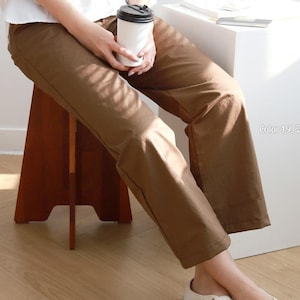 May include: A pair of solid brown trousers with a straight-leg cut and a clean, simple design. The pants feature a smooth, matte finish and a standard waistband, providing a neutral and versatile look for various outfits and daily wear.