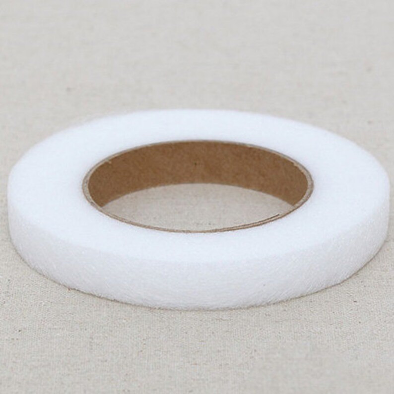 May include: A roll of white, non-woven interfacing fabric. The interfacing is a ring shape with a brown cardboard core. The fabric is thick and appears to be soft. The roll is sitting on a light beige surface.