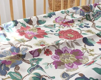 May include: A white fabric sheet featuring a repeating floral pattern with large blossoms in shades of red, purple, blue, and green. The textile displays intricate botanical illustrations of flowers and leaves spread across the surface.