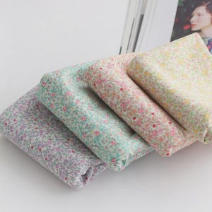 May include: Four folded fabric squares in pastel colors: lavender, mint green, pink, and pale yellow. Each fabric is covered in a delicate floral pattern with tiny flowers in shades of red, pink, and yellow.