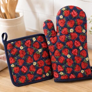 Pu&ograve; includere: Un guanto da forno trapuntato e una presina quadrata con sfondo blu scuro e un motivo ripetuto di fragole rosse, foglie verdi e piccoli fiori bianchi. Entrambi gli articoli presentano un bordo in tessuto blu scuro e un occhiello.