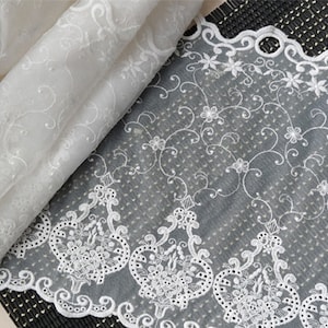 May include: White embroidered lace trim with a delicate floral pattern. The lace has a scalloped edge and is perfect for adding a touch of elegance to any project.
