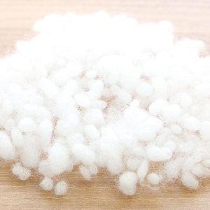 May include: A pile of fluffy, white polyester fiberfill, ideal for stuffing pillows, cushions, or plush toys. The soft, cloud-like material is shown against a light wood grain surface.