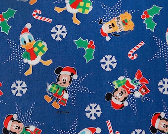 Puede incluir: Una tela azul con un patrón repetido de Mickey Mouse, Donald Duck y Pluto vestidos de Papá Noel y sosteniendo regalos. El fondo es azul con lunares blancos y copos de nieve.