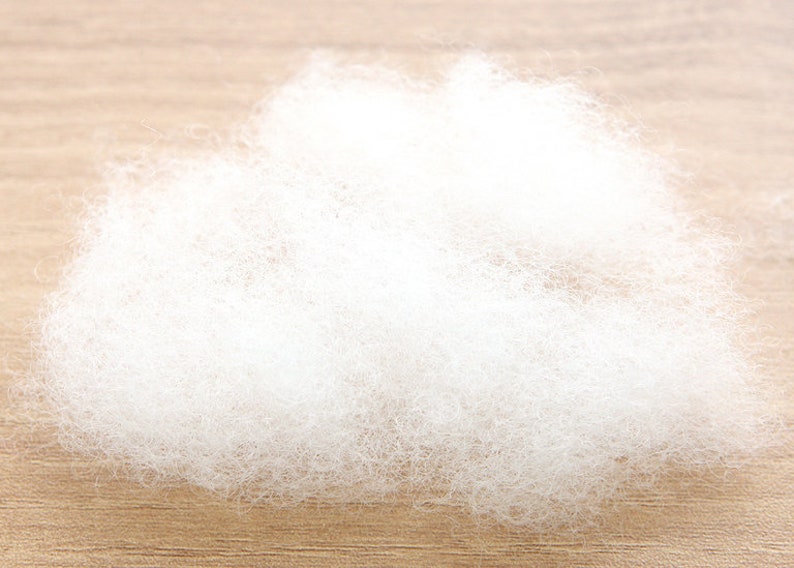 May include: A fluffy cloud of white polyester fiberfill, ideal for stuffing pillows, cushions, or craft projects. The soft, lightweight material is shown against a light brown wooden surface.
