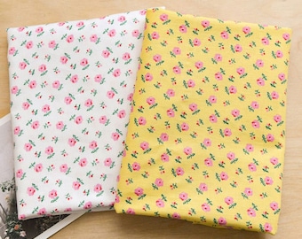 May include: Two folded pieces of fabric featuring a repeating pattern of small pink flowers with green stems and leaves. One piece of fabric has a white background, while the other piece of fabric has a bright yellow background.