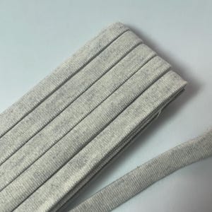 Pu&ograve; includere: Un rotolo di nastro in tessuto o bordatura color grigio chiaro m&eacute;lange. Il materiale presenta una consistenza morbida e punteggiata con una trama uniforme e un design a bordo piatto e piegato. Il nastro &egrave; avvolto in vari strati sovrapposti.