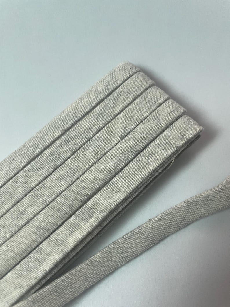 Pu&ograve; includere: Un rotolo di nastro in tessuto o bordatura color grigio chiaro m&eacute;lange. Il materiale presenta una consistenza morbida e punteggiata con una trama uniforme e un design a bordo piatto e piegato. Il nastro &egrave; avvolto in vari strati sovrapposti.